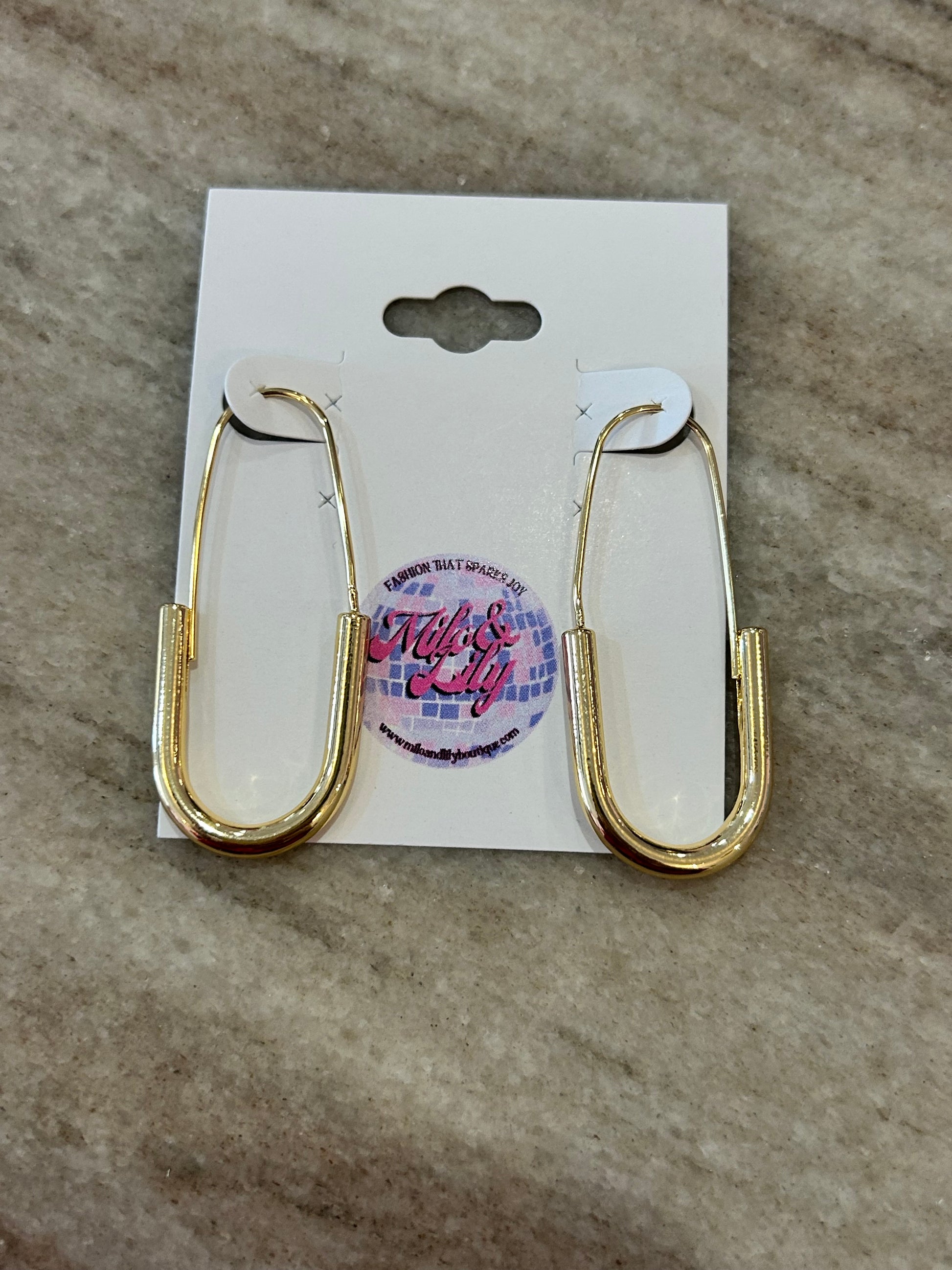 Gold geometric hoop earrings on display card, women's jewelry on stone surface