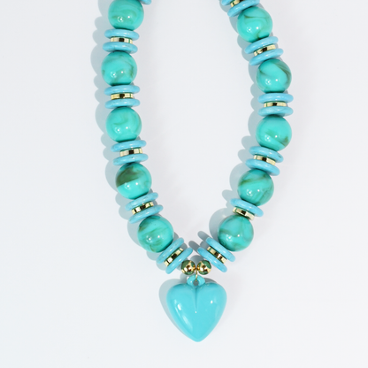 Turquoise beaded necklace with gold accents and heart pendant on white background