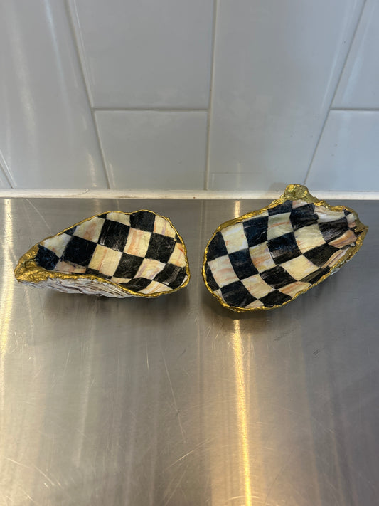 Two decorative oyster shells with black and white checkered pattern and gold trim on metal surface