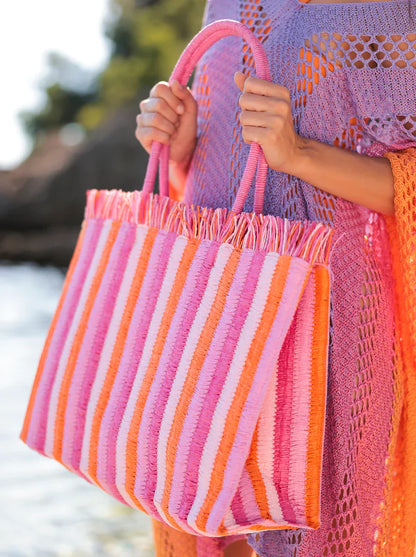 Woman holding a pink and orange striped woven tote bag outdoors in summer