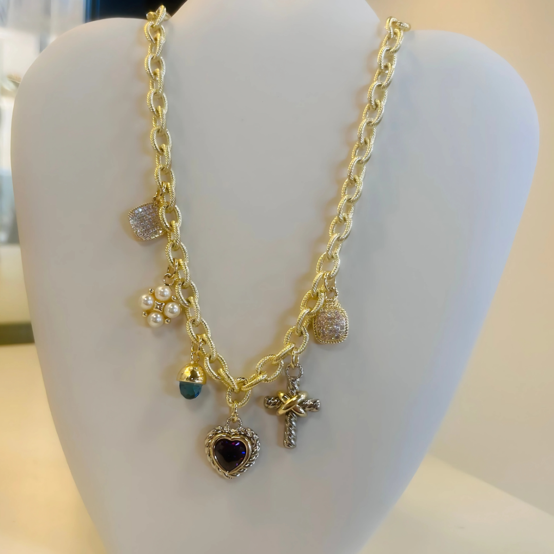 Gold chain necklace with multiple charms including a cross, heart, pearls, and gemstones.