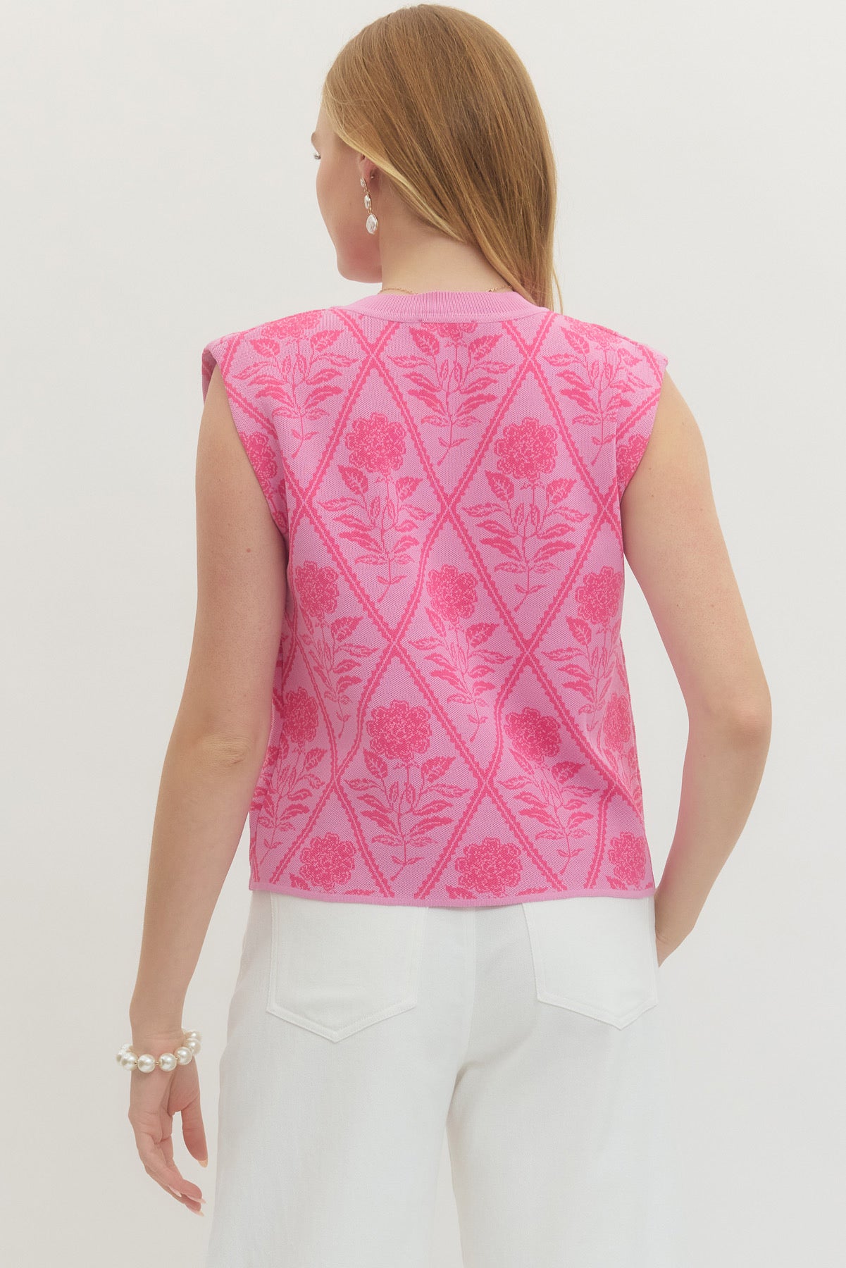 Woman wearing pink floral sleeveless knit top and white pants, back view