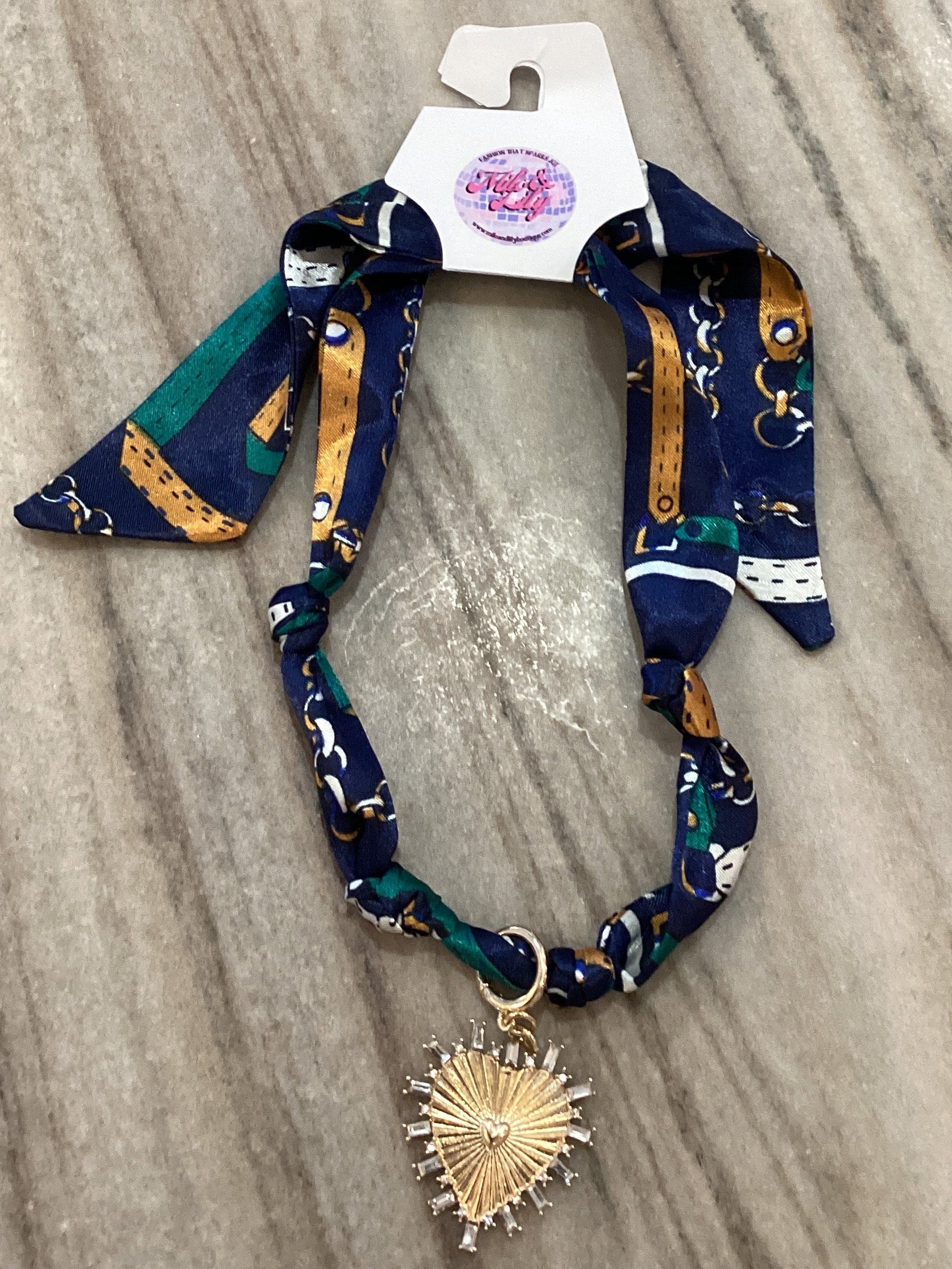 Patterned navy scarf necklace with gold heart pendant on marble background