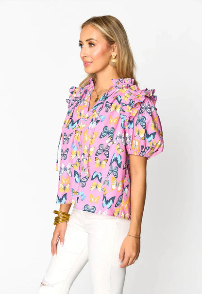 Woman wearing a pink butterfly print blouse with ruffle sleeves and white jeans