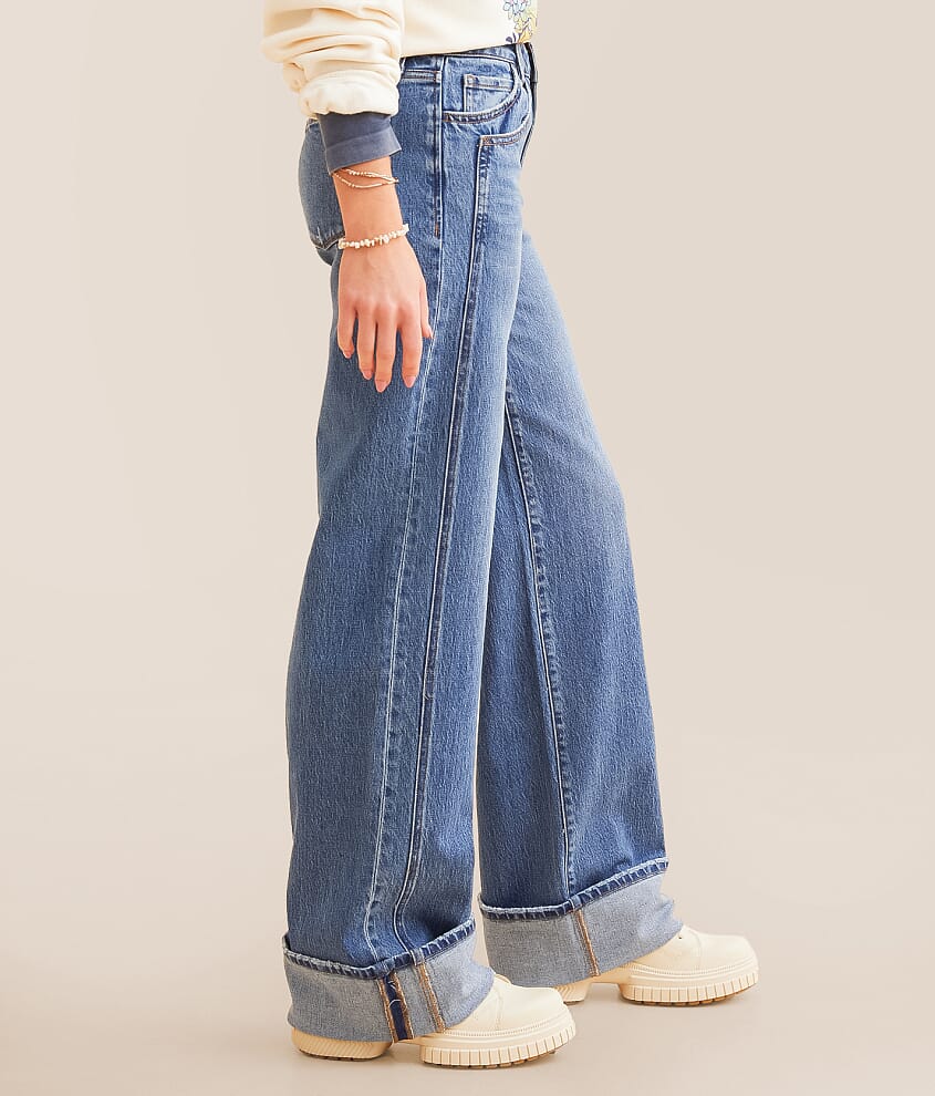 Woman wearing wide leg cuffed denim jeans and white sneakers, side view