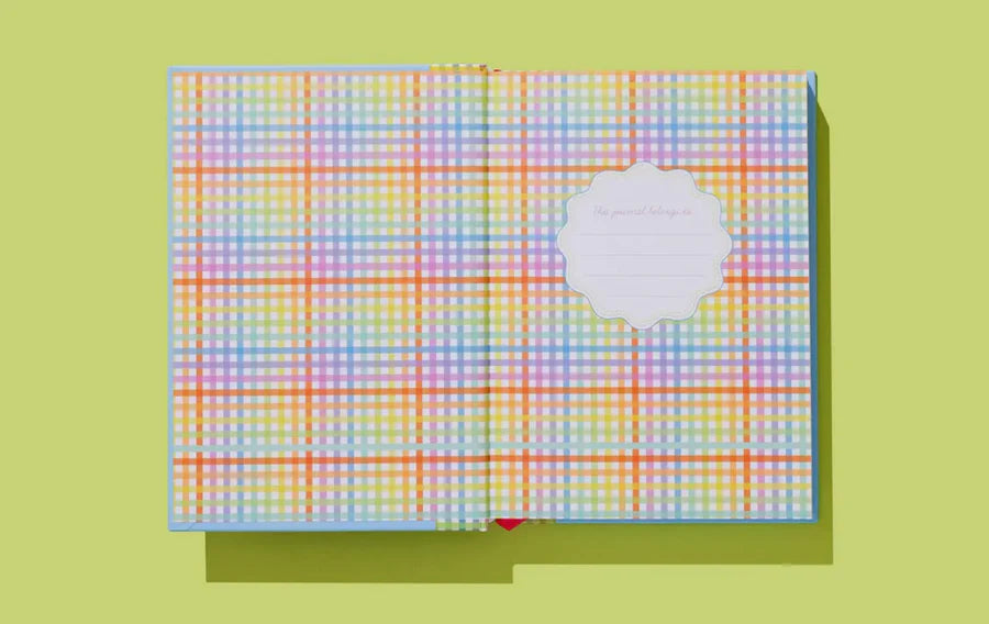 Open notebook with colorful pastel plaid pattern on inside cover, blank label, on green background