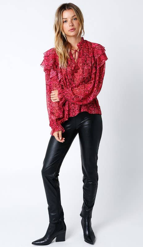 Woman wearing a red floral ruffle blouse and black faux leather pants with ankle boots