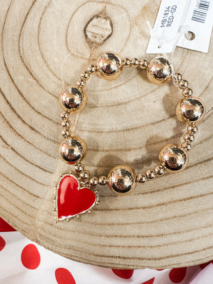 Gold beaded bracelet with a red heart charm on wood, women's jewelry accessory