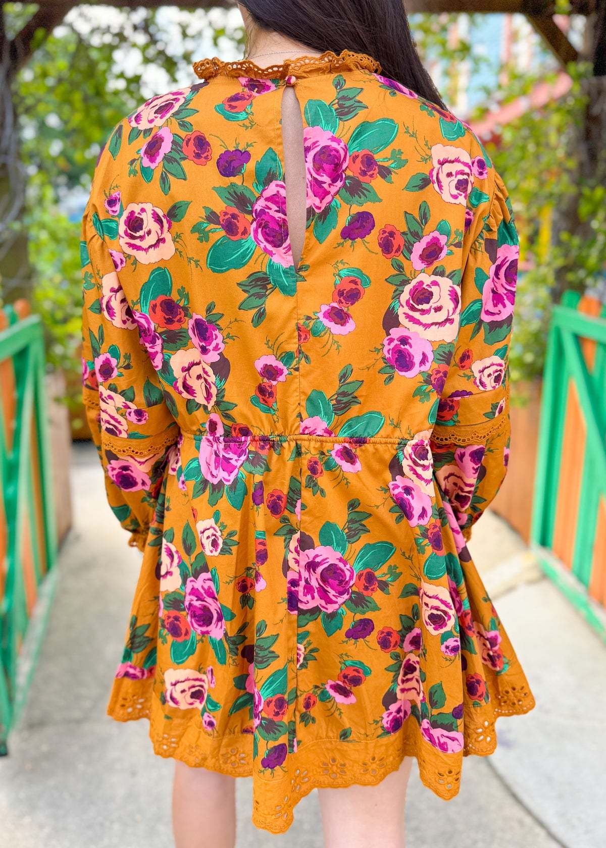 Back view of woman in a yellow floral dress with pink and green rose print and lace trim