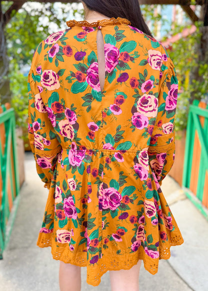Back view of woman in a yellow floral dress with pink and green rose print and lace trim