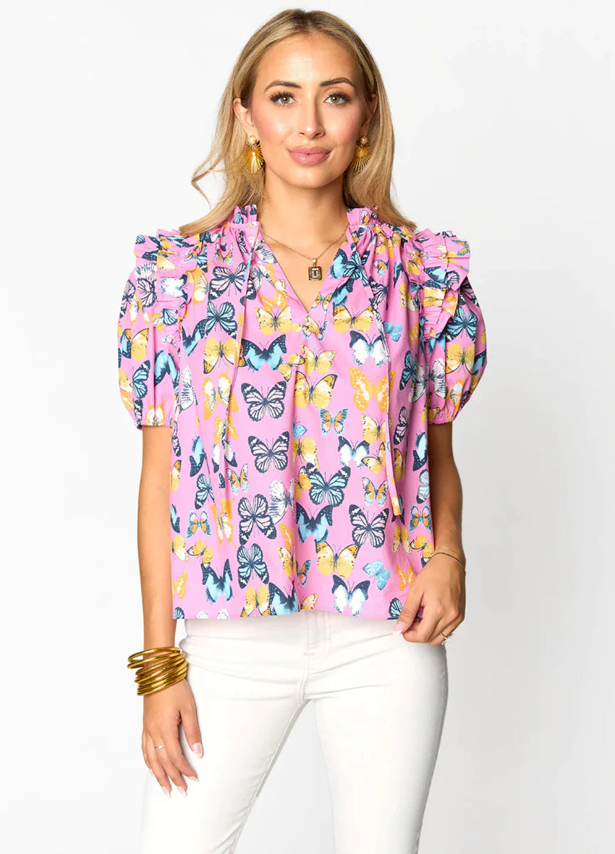 Woman wearing a pink butterfly print blouse with ruffled sleeves and white jeans