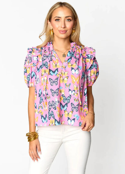 Woman wearing a pink butterfly print blouse with ruffled sleeves and white jeans