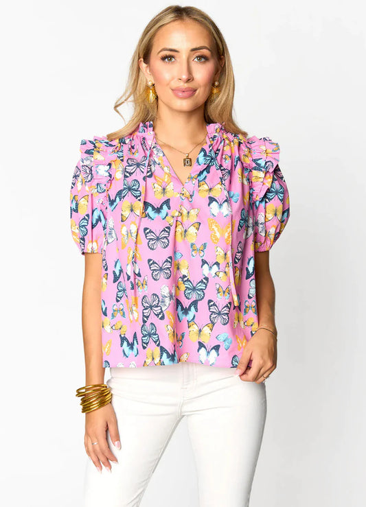 Woman wearing a pink butterfly print blouse with ruffled sleeves and white jeans