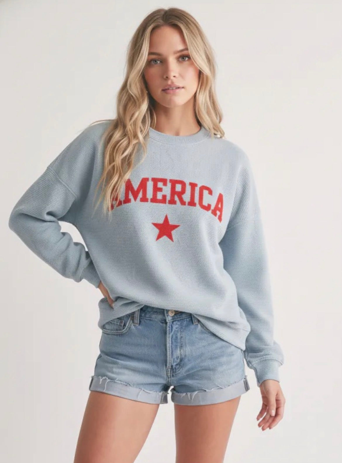Woman wearing a light blue sweatshirt with 'AMERICA' and a red star design on a plain background