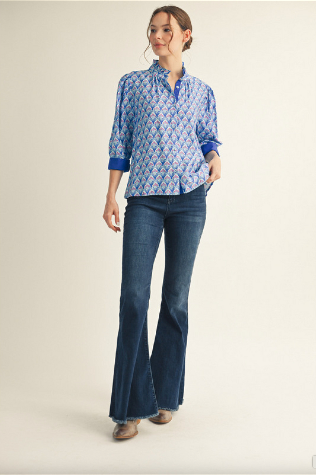 Woman wearing patterned blue blouse with cuffed sleeves and dark wash flared jeans
