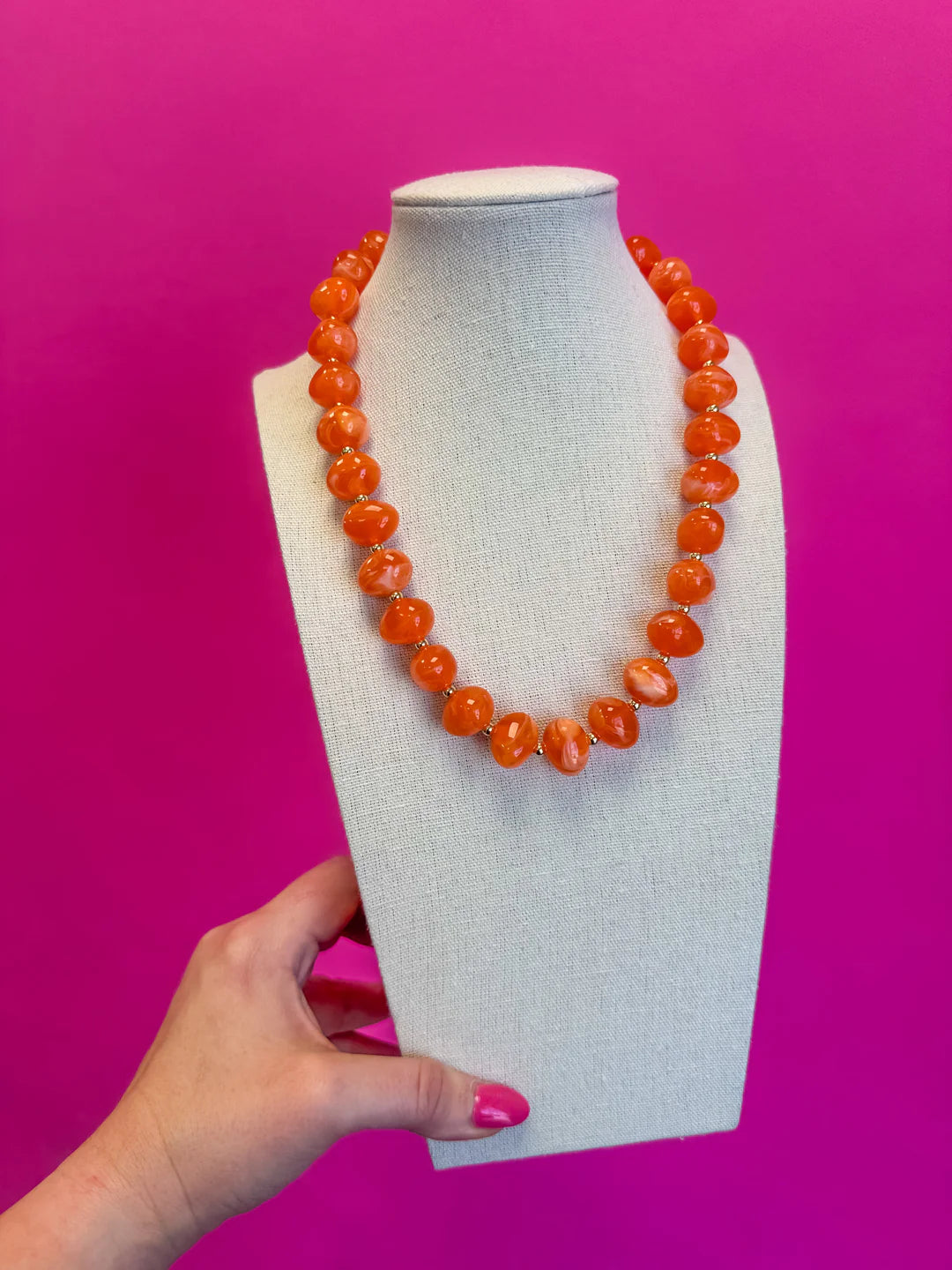 Orange beaded necklace on a mannequin bust against a pink background