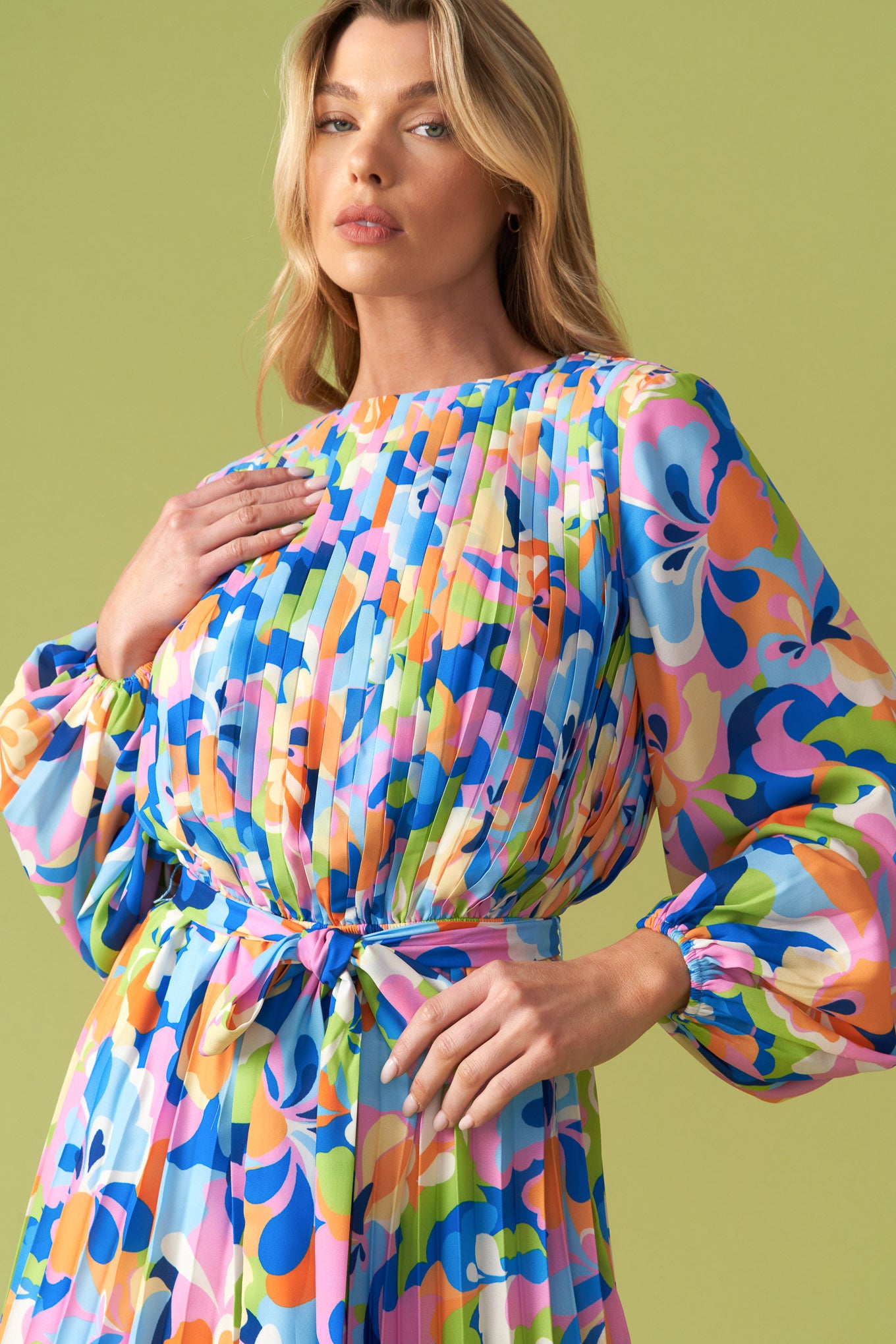 Vibrant floral pleated long sleeve romper with waist tie belt, featuring a bold multicolor print in blue, pink, orange, and green. Flowy, lightweight fabric with a flattering cinched waist, balloon sleeves, and an elegant round neckline. Perfect for stylish, playful fashion lovers at Milo & Lily Boutique.
