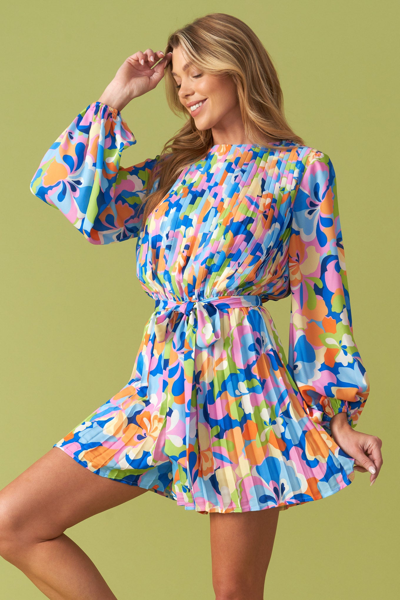 Vibrant floral pleated long sleeve romper with waist tie belt, featuring a bold multicolor print in blue, pink, orange, and green. Flowy, lightweight fabric with a flattering cinched waist, balloon sleeves, and an elegant round neckline. Perfect for stylish, playful fashion lovers at Milo & Lily Boutique.