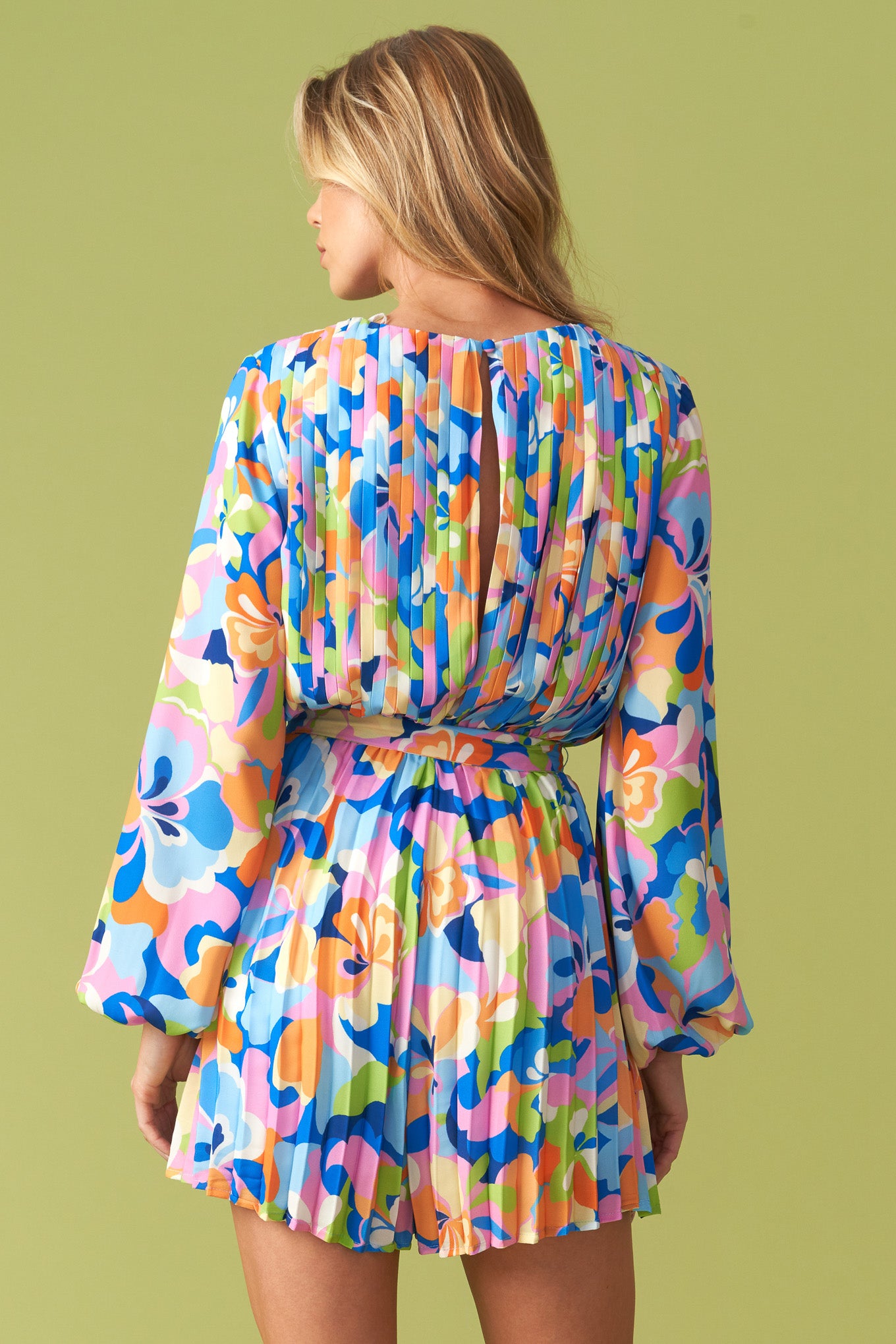Vibrant floral pleated long sleeve romper with waist tie belt, featuring a bold multicolor print in blue, pink, orange, and green. Flowy, lightweight fabric with a flattering cinched waist, balloon sleeves, and an elegant round neckline. Perfect for stylish, playful fashion lovers at Milo & Lily Boutique.