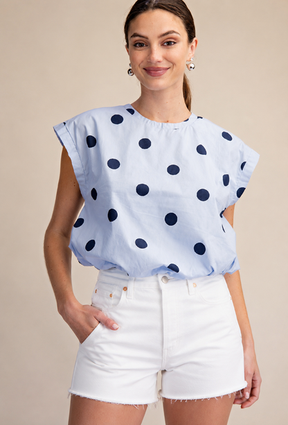 Woman wearing a light blue blouse with dark polka dots and white shorts on a beige background