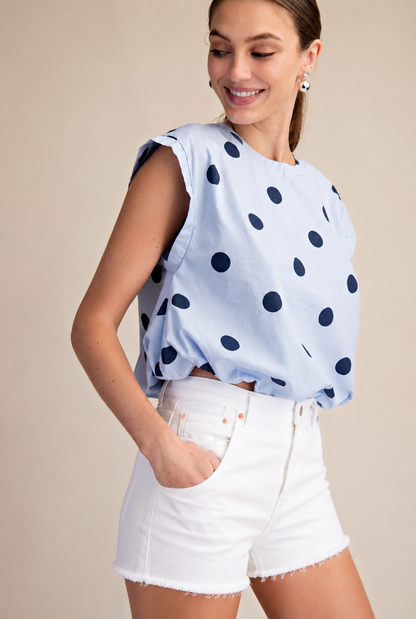 Woman wearing a light blue top with dark polka dots and white shorts on a beige background