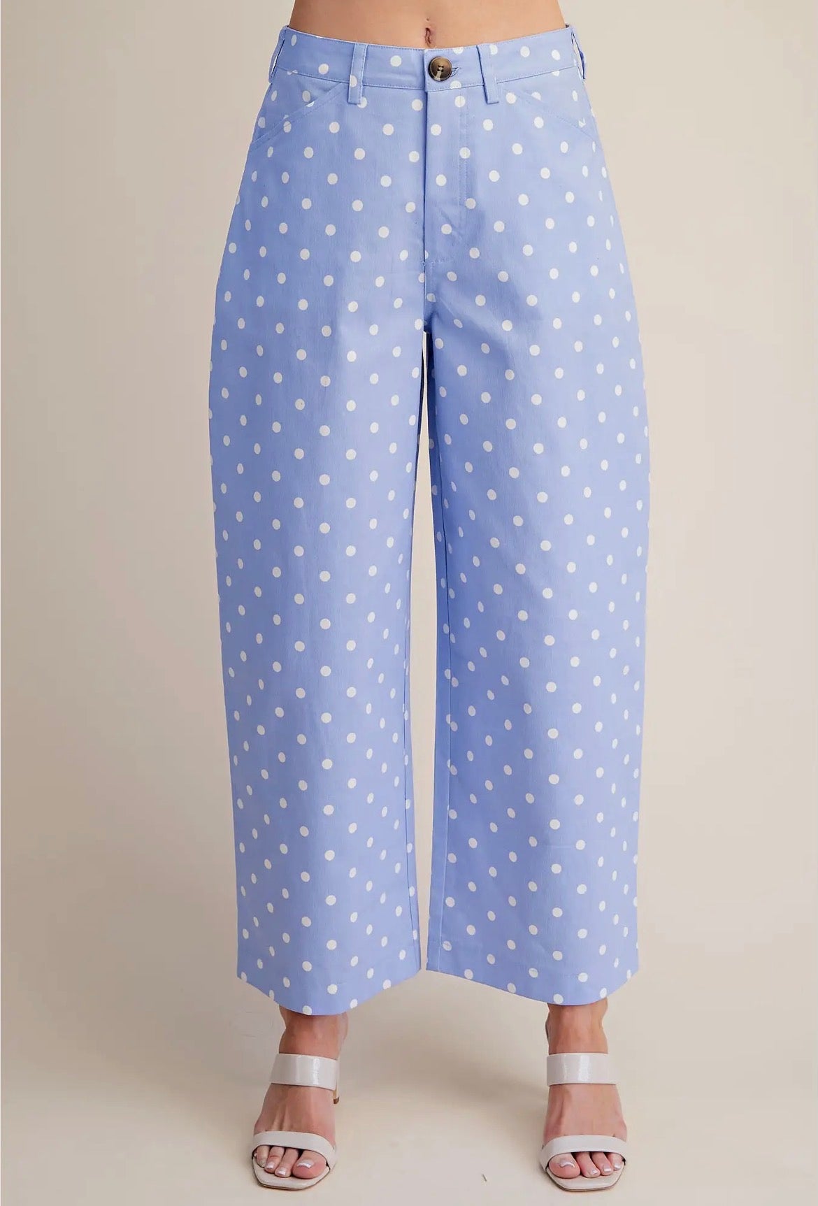 A person wearing light blue cropped wide-leg pants with a white polka dot pattern, paired with white heeled sandals, against a plain beige studio background.