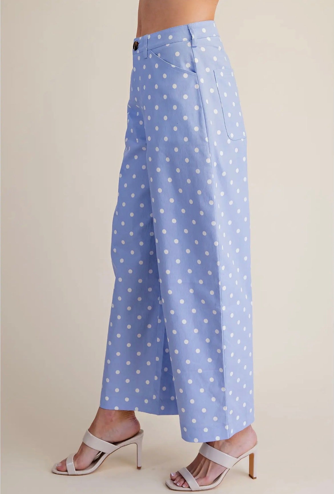 A person wearing light blue wide-leg cropped pants with a white polka dot pattern, paired with white heeled sandals, shown against a plain beige studio background.