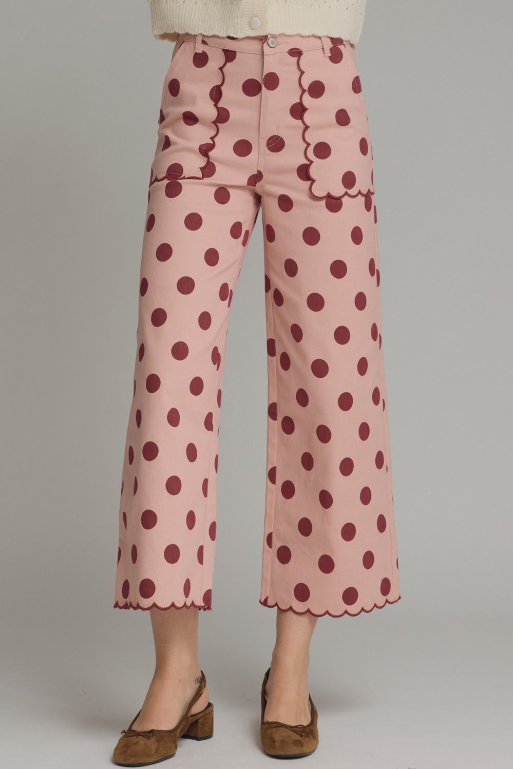 Pink pants with red polka dots worn by a person on a gray background