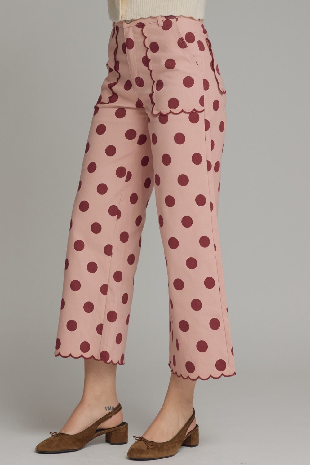 Pink pants with brown polka dots worn by a person on a gray background