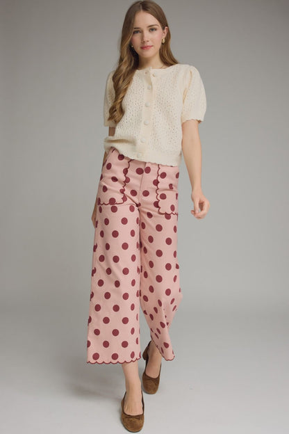 Woman wearing a cream blouse and pink polka dot pants on a gray background