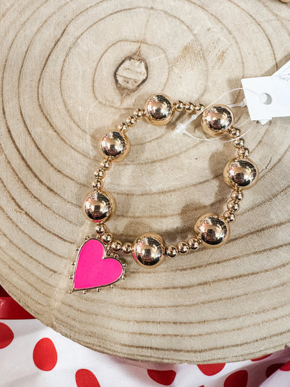 Gold beaded bracelet with a pink heart charm on a wooden background, jewelry accessory