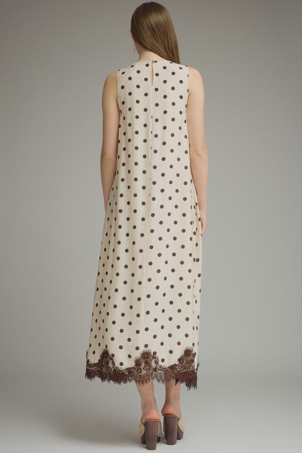 Woman wearing a polka dot dress with lace trim on a plain background