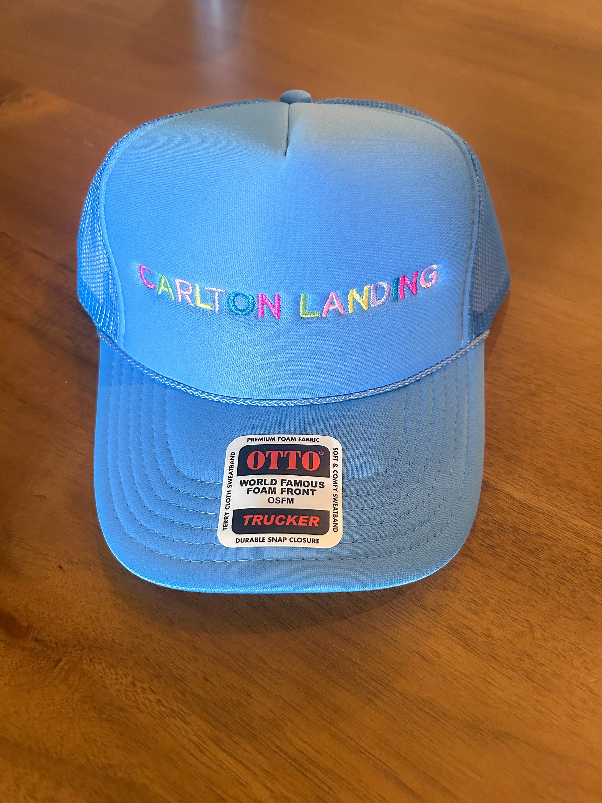 Blue trucker hat with 'Carlton Landing' text on a wooden surface