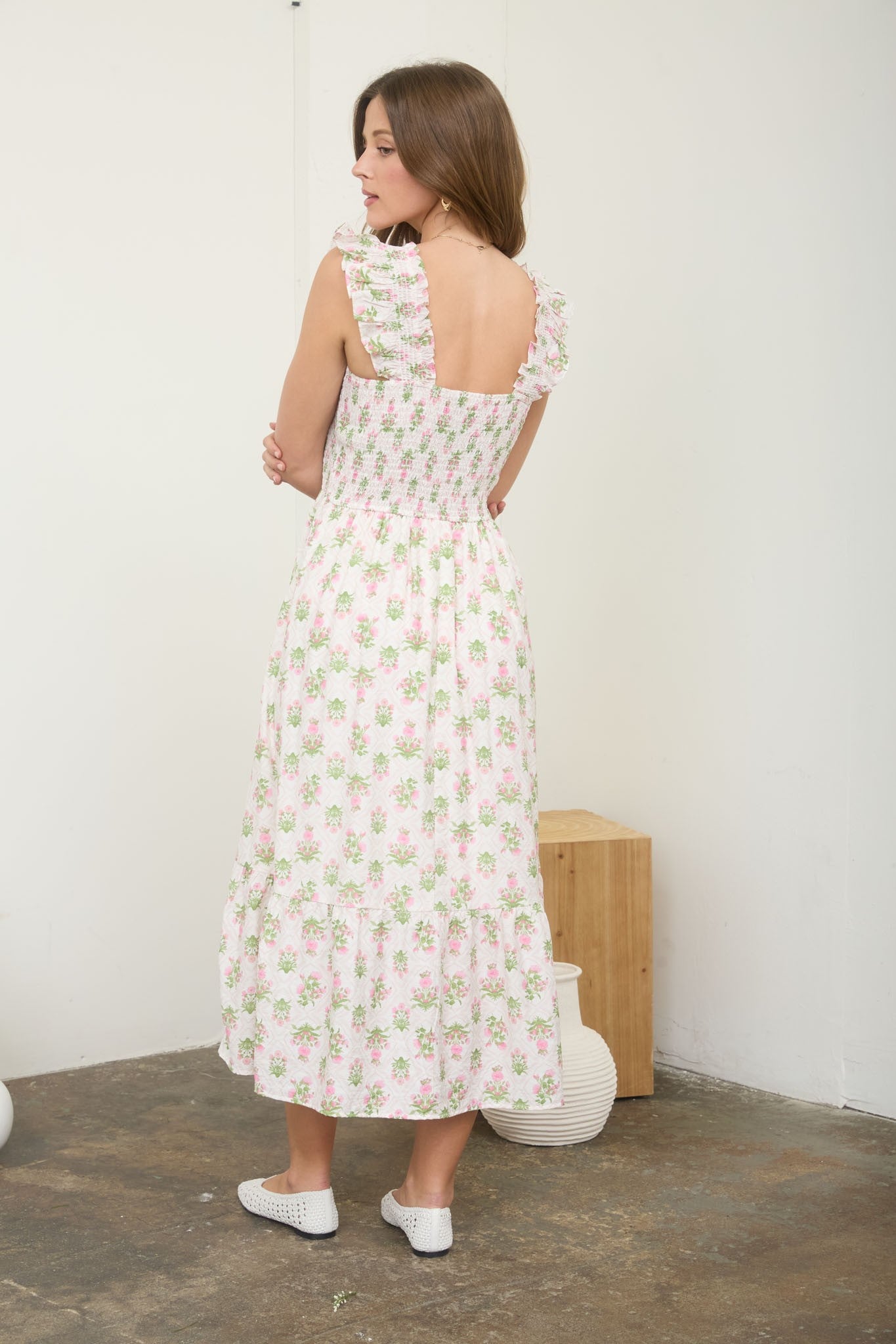 Woman wearing a floral dress standing against a white wall.