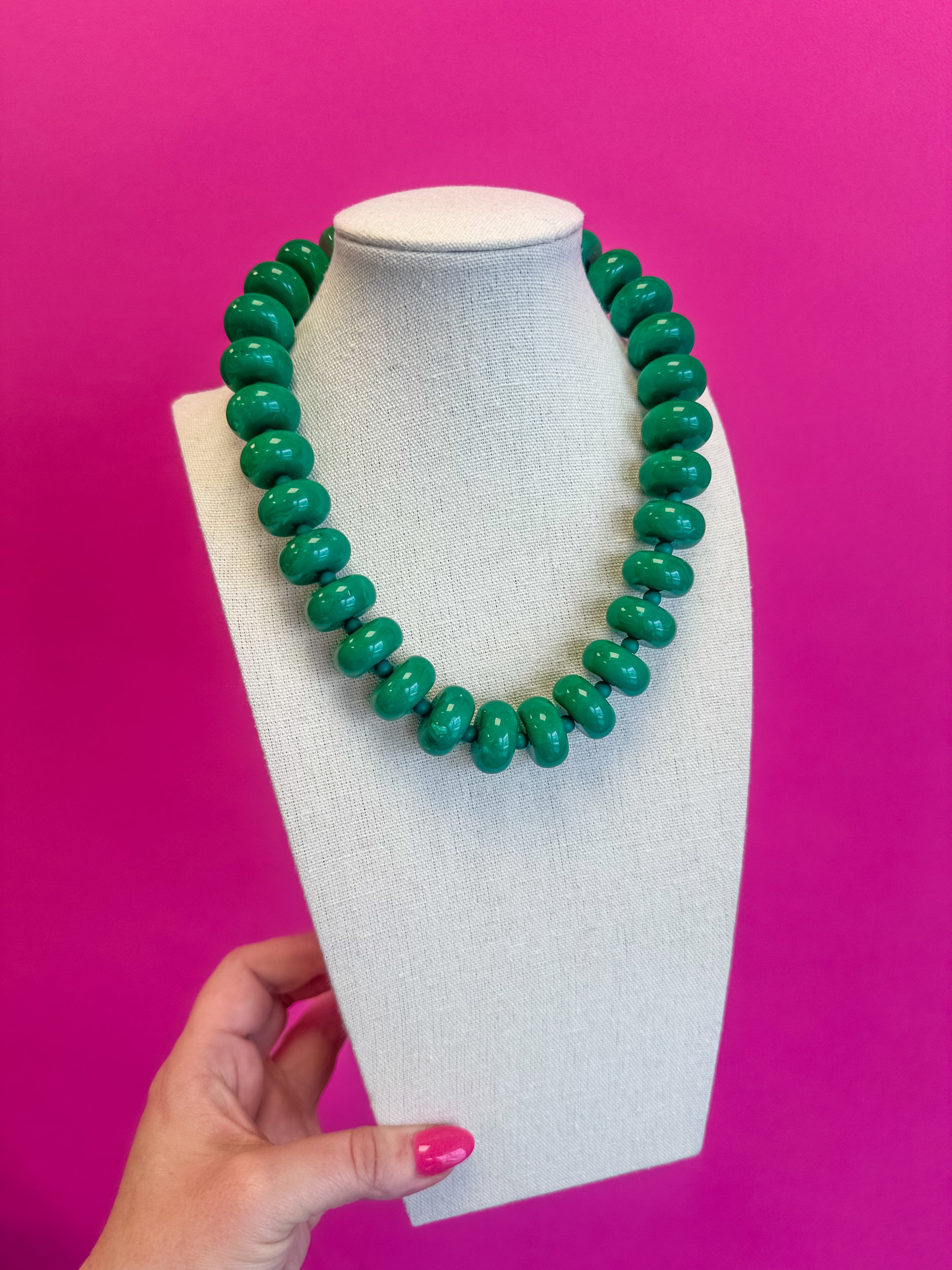 Green beaded necklace on a mannequin bust against a pink background