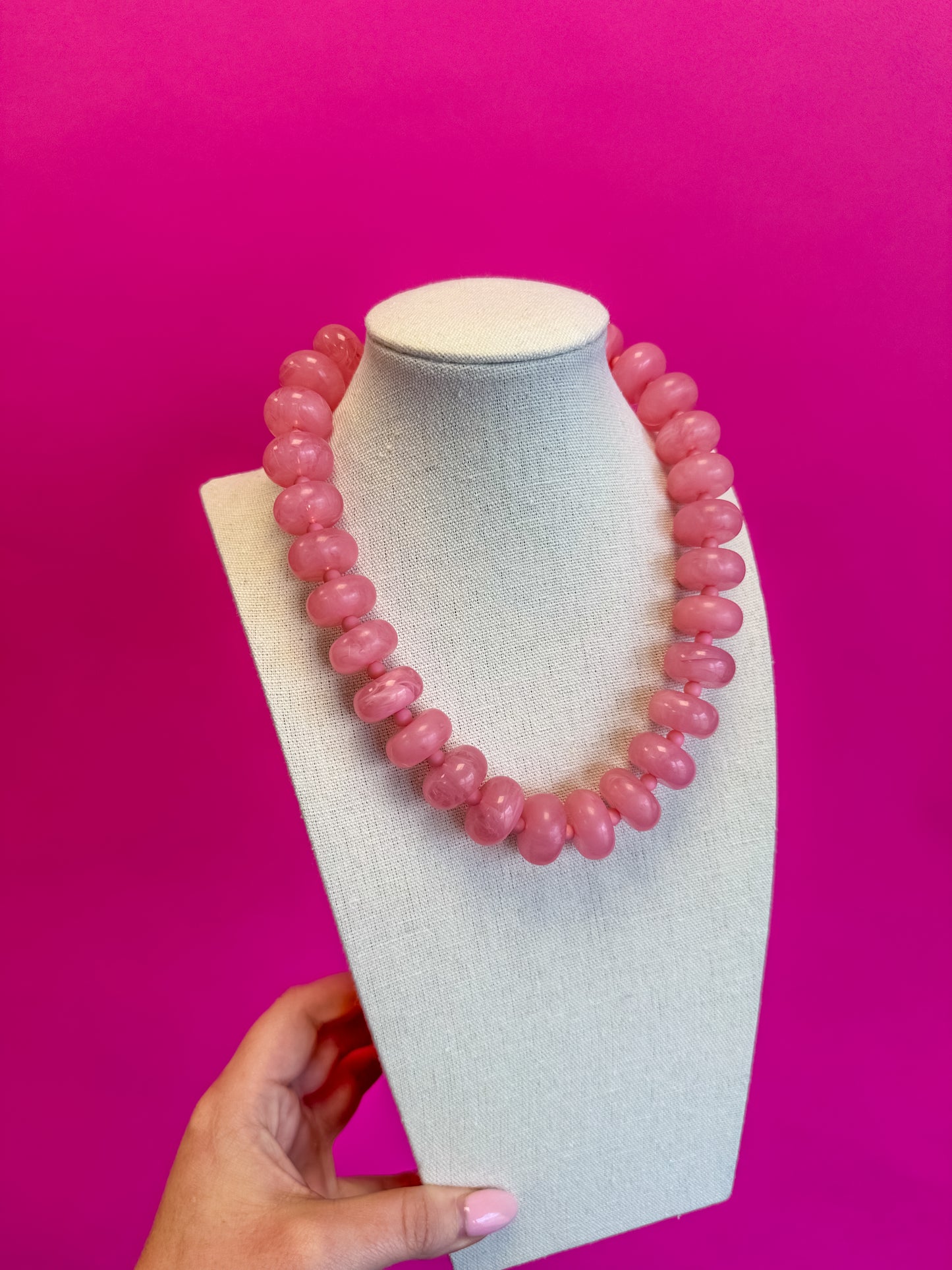 Pink beaded necklace on a white bust against a pink background