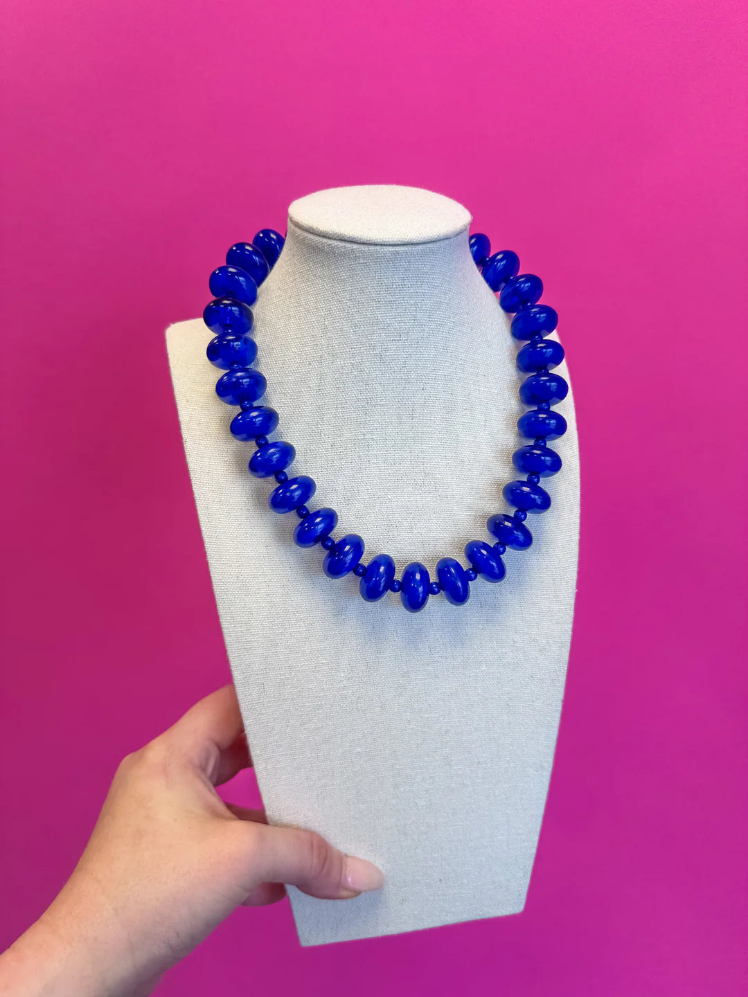 Blue beaded necklace on a white mannequin bust against a pink background
