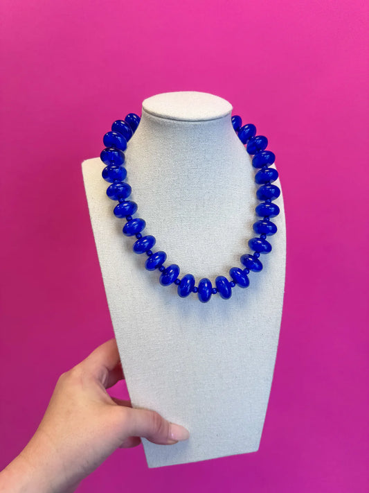 Blue beaded necklace on a white mannequin bust against a pink background