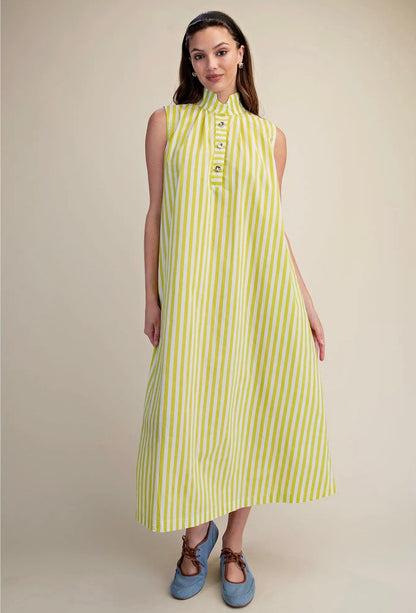 A woman modeling a sleeveless midi dress with vertical lime green and white stripes, featuring a mock neck and decorative button details at the collar, paired with blue shoes against a solid beige background.