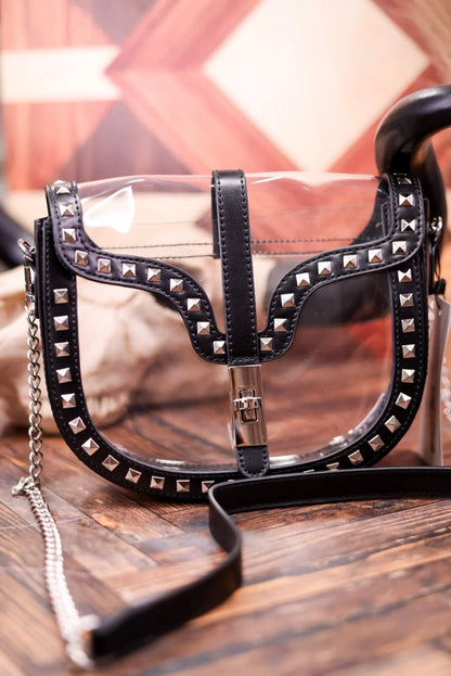A clear vinyl shoulder bag with black faux-leather trim, silver pyramid studs, and a silver chain strap, resting on a wooden surface.