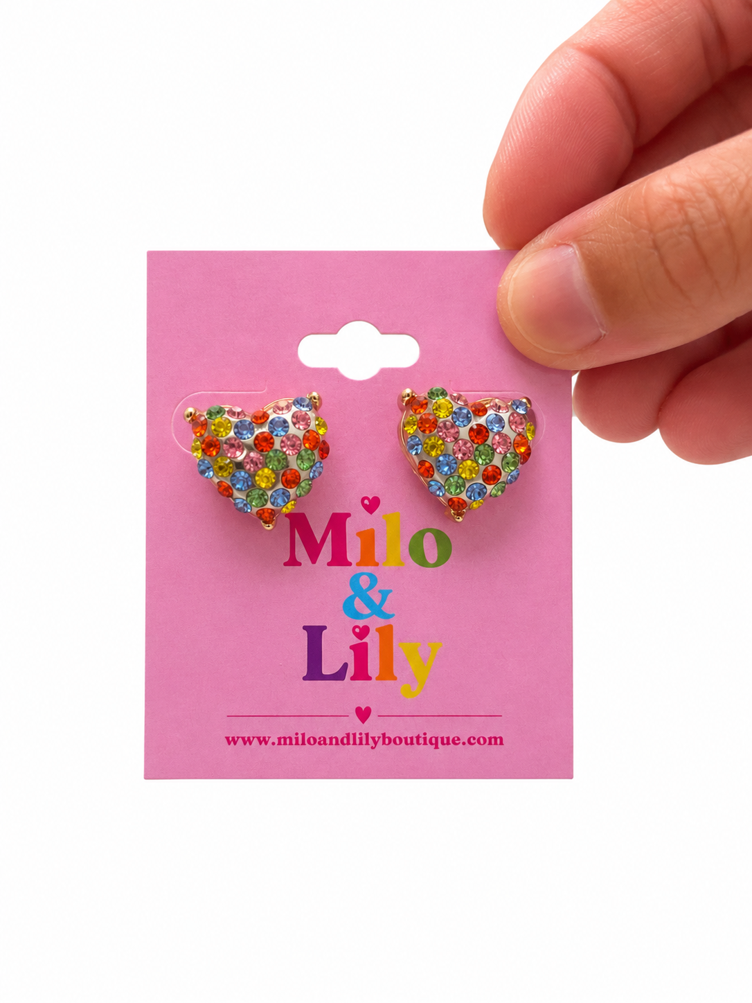 A hand holding a pink card displaying two heart-shaped stud earrings covered in colorful rhinestones. The card is branded 'Milo & Lily'.