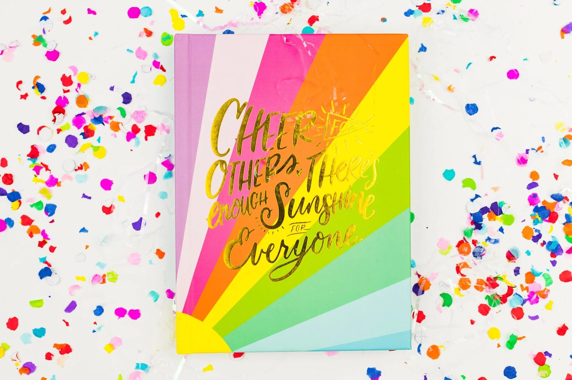 Rainbow striped greeting card with gold text, surrounded by colorful confetti on white background.