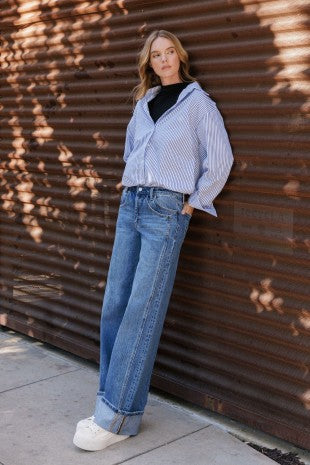 Woman wearing relaxed striped blouse, black top, and wide-leg denim jeans with white sneakers