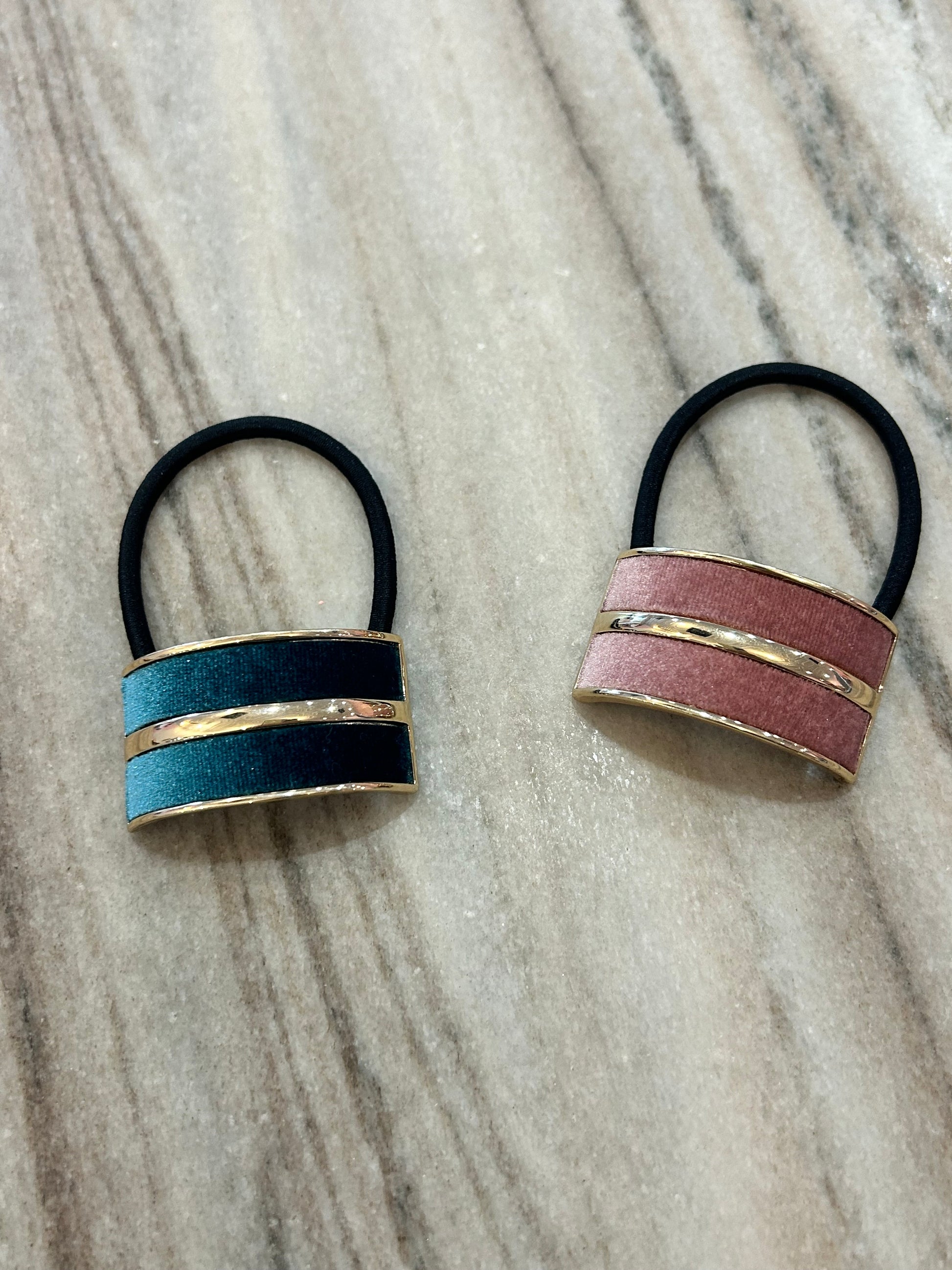 Two elastic hair ties with metallic gold and colored bands, one teal, one pink, on marble surface.