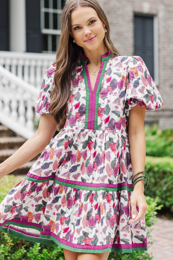 Woman wearing a short puff sleeve floral dress with pink, purple, and green accents outdoors.