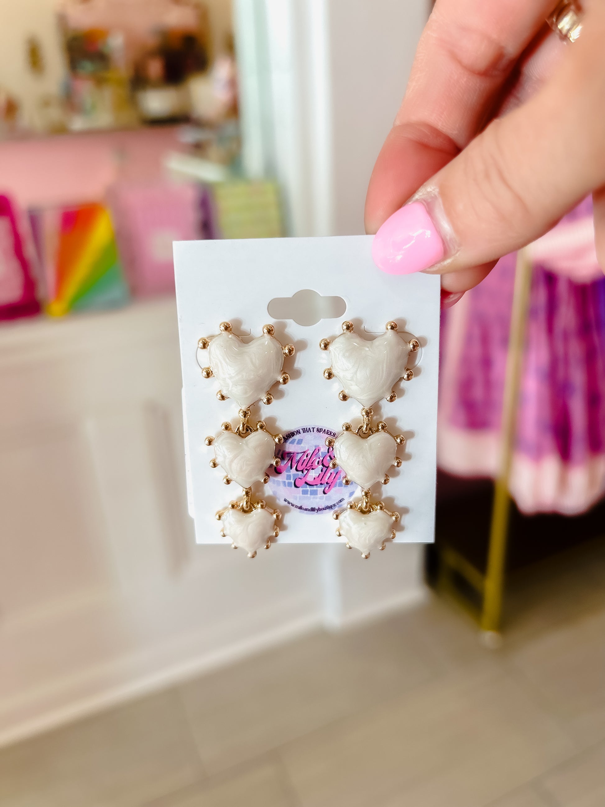 Gold-trimmed white heart earrings with textured surface, held in a boutique setting