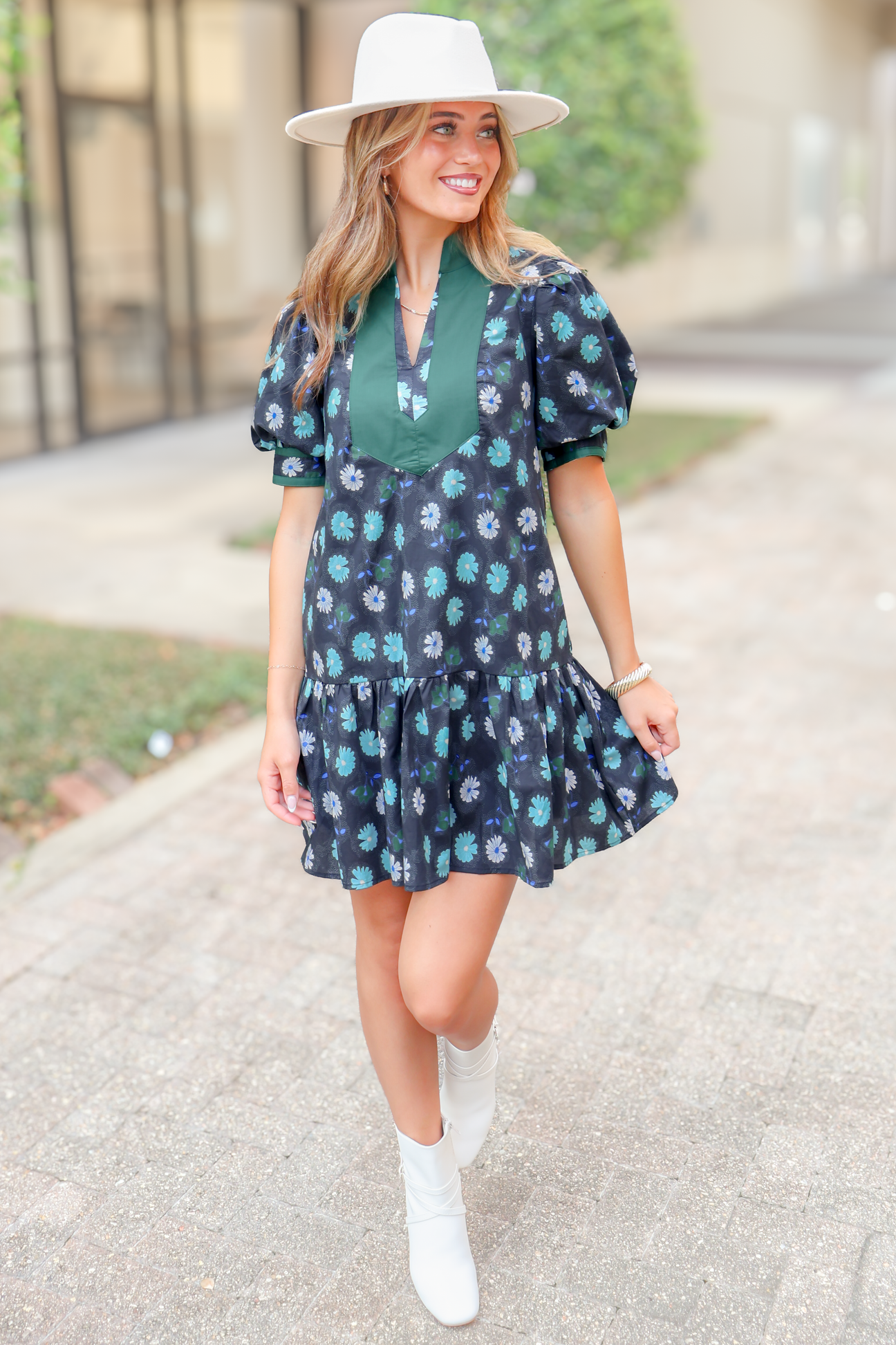 Woman in floral mini dress with puff sleeves, white hat, and white ankle boots outdoors