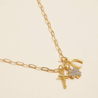 Gold chain necklace with cross, rhinestone clover, and wishbone charms on beige background
