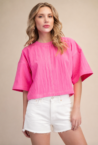 Woman wearing a bright pink top and white shorts on a beige background