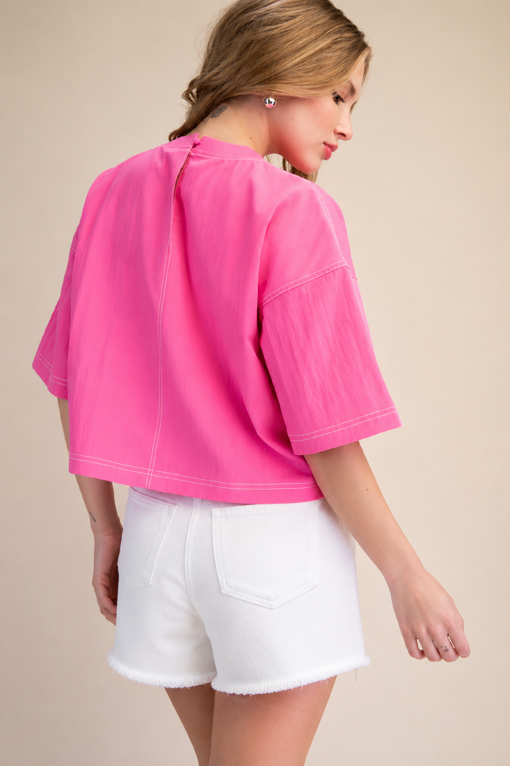 Woman wearing a bright pink top and white shorts on a beige background